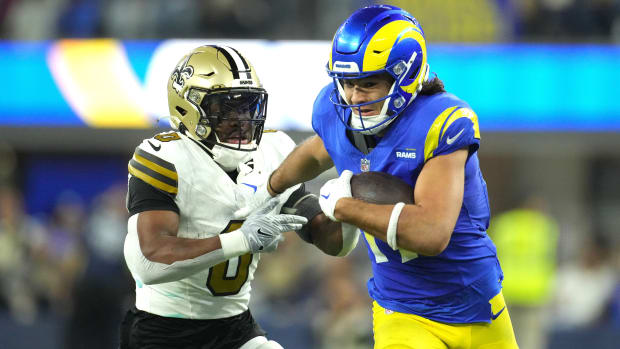 Puka Nacua runs with the ball in one hand as he reaches behind him to block a Saints player chasing him